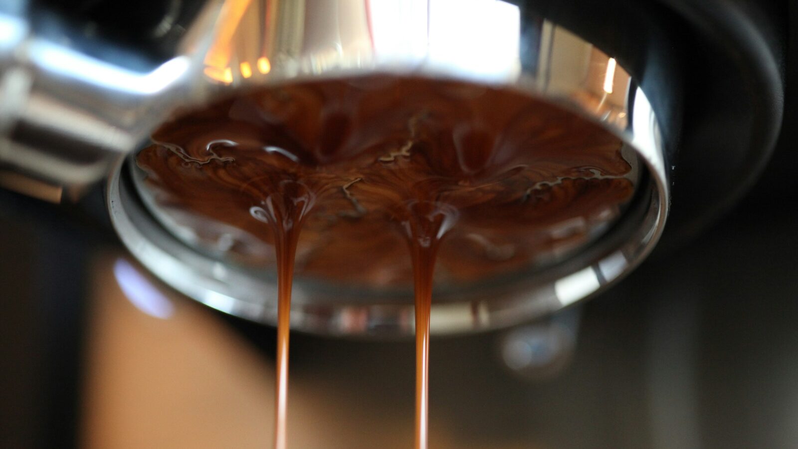 Espresso escorrendo de um porta-filtro sem fundo para dentro da xícara.